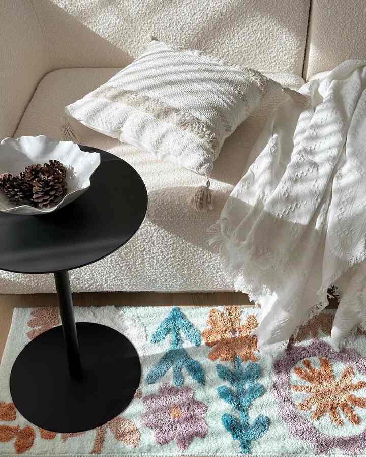 White-toned living room featuring a textured sofa with cushions and a floral patterned rug creating a cozy natural atmosphere