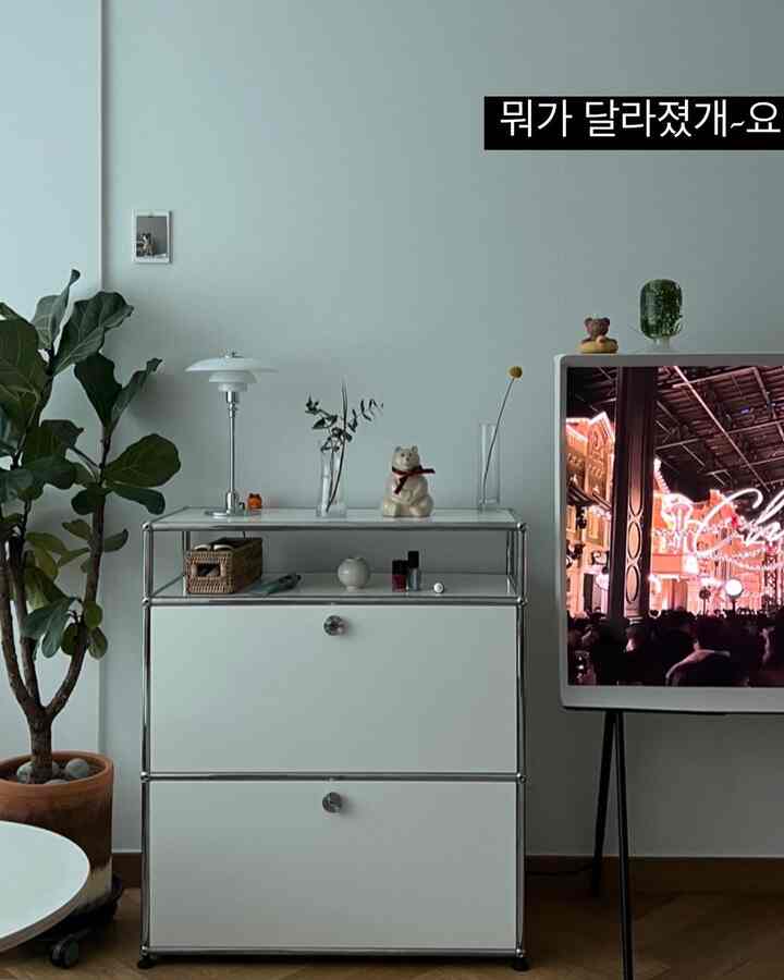 A white and wood tone living room featuring a sleek cabinet and a large plant, creating a simple modern interior