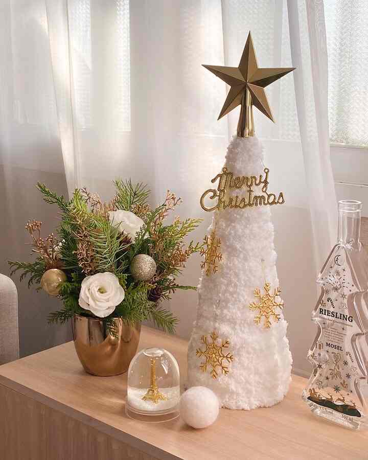 ホワイトとゴールドのクリスマス装飾が置かれた木製テーブル、透けるカーテンを背景にした温かみのある印象的な空間