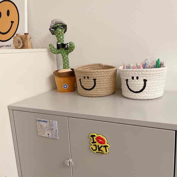 Light beige and white toned kids' room featuring smile-patterned storage baskets and a dancing cactus on a neat metal cabinet