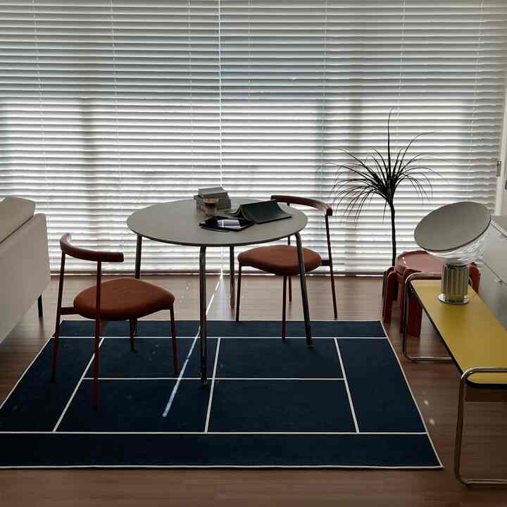 ホワイトのブラインドを背景に、イエローベンチと円形テーブル、ベージュのソファが配置されたナチュラルなリビング空間