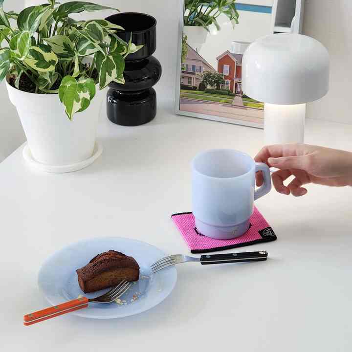 White-toned clean home cafe space featuring a plant, table lamp, mug, and dessert plate with a simple atmosphere