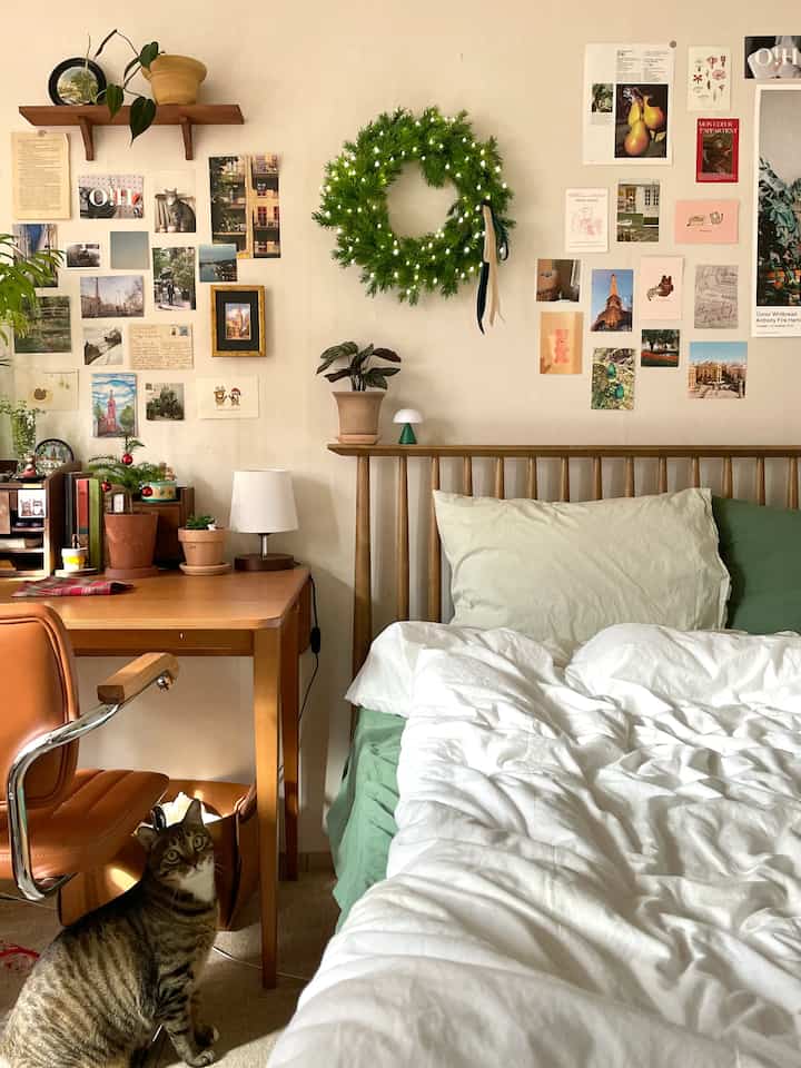Natural toned bedroom featuring wooden furniture, green plants, and a Christmas wreath with photos on the wall creating a cozy atmosphere
