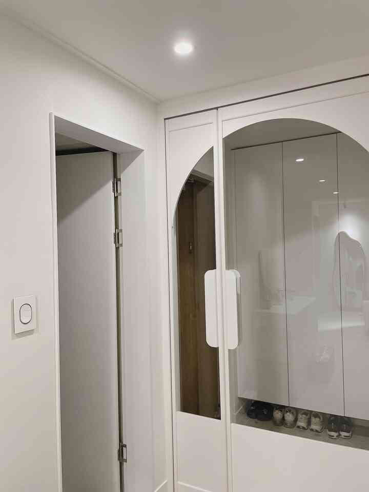 White-toned entrance space featuring arched glass shoe cabinet and sleek lighting with clean modern interior