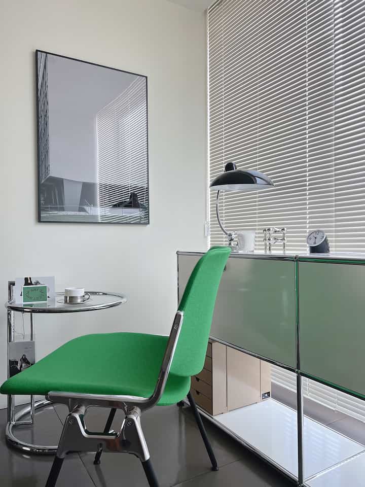 Dining room corner with white walls and blinds background, featuring a green chair and metallic storage cabinets in a modern setting