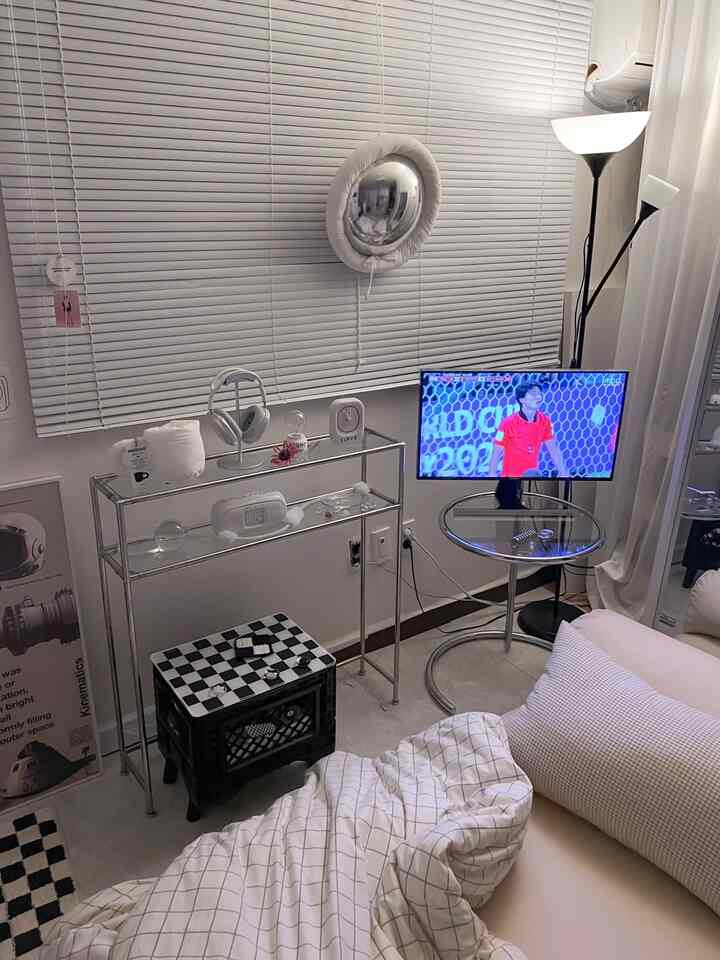 白とグレーのトーンのワンルームリビング、ミッドセンチュリーモダンの金属家具とブラインド、サイドテーブル、テレビが配置された印象的な空間