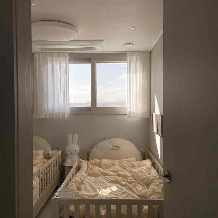 白とベージュの色調の子供部屋、二つのベビーベッドとウサギのムードライトが配置された雰囲気のある空間