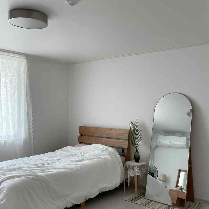 White and wood-tone bedroom featuring a simple bed and an arched oversized mirror in a minimalistic space