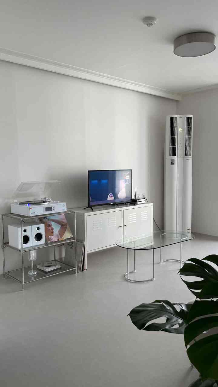 Modern living room in white tone featuring transparent glass table, cabinet, and air conditioner in a clean space