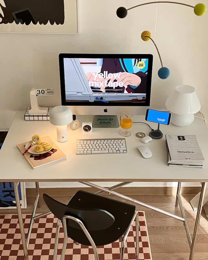 White-toned home office space featuring a white desk, black chair, colorful mobile, and cozy lighting accessories