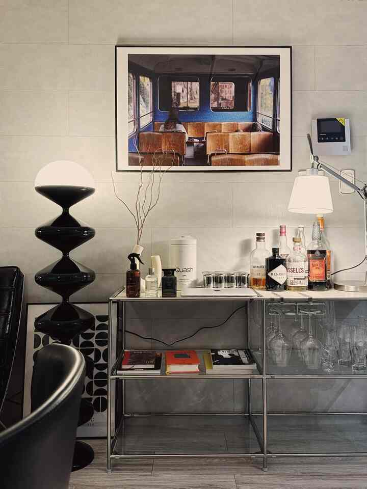 Black and white toned living room featuring modern metal shelving with assorted liquors and lighting for a home bar setup