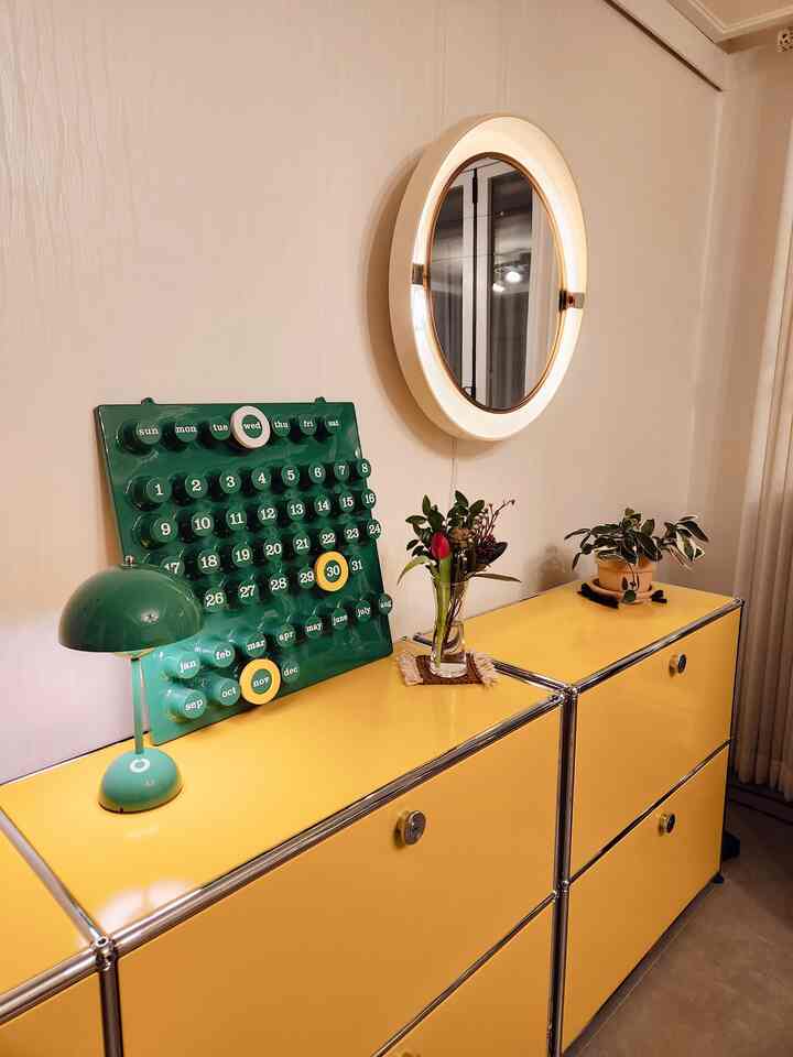 Warm living room featuring bright yellow sideboards topped with a green calendar, a vase of flowers, and a round illuminated mirror