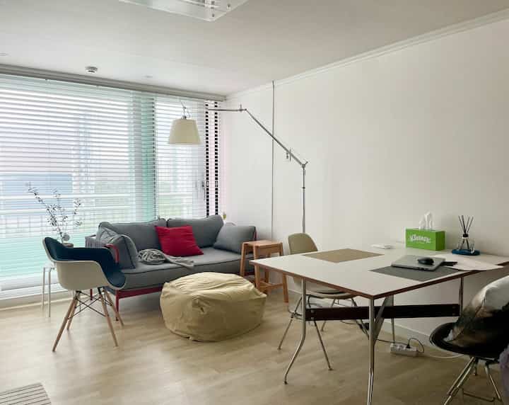 White and light brown toned living room featuring modern sofa, armchair, and a desk set up for remote work in a clean layout