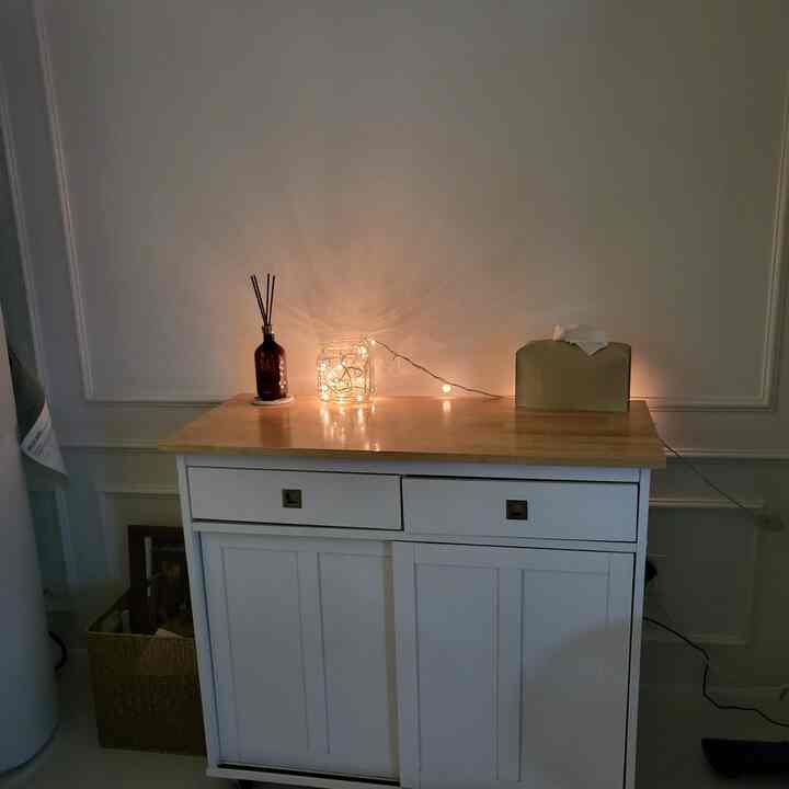 白色の収納キャビネットが配置された空間、上部にディフューザーとストリングライトが柔らかな雰囲気を演出するインテリア