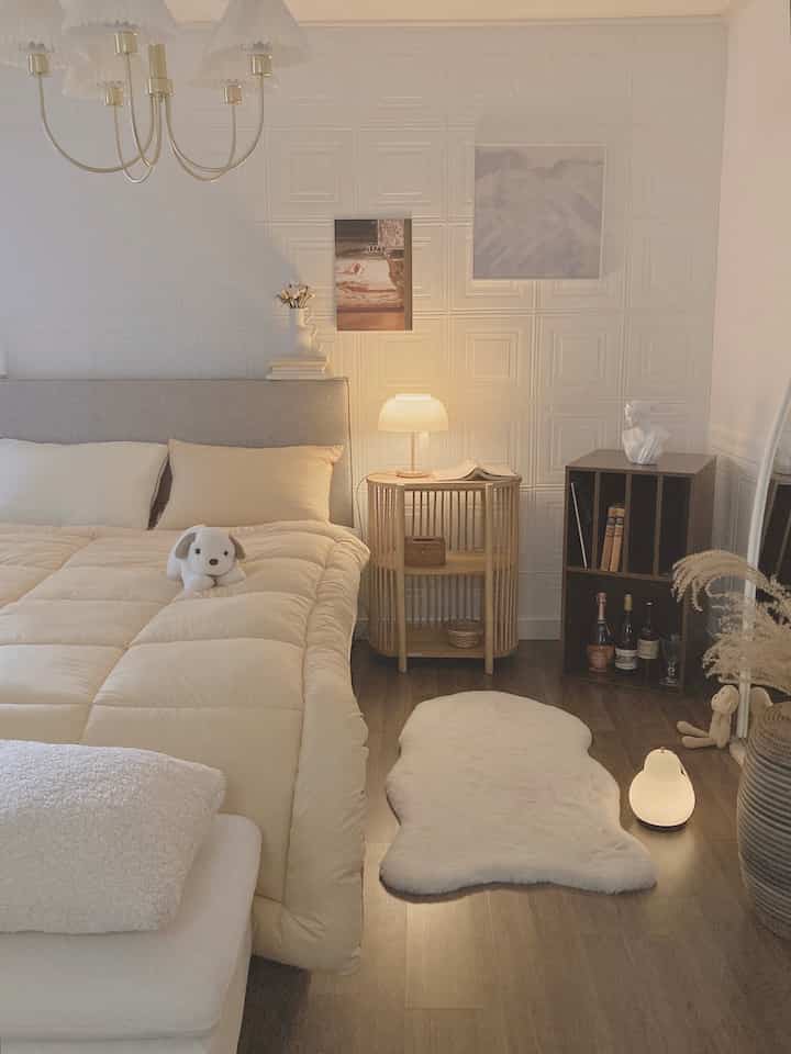 A white and beige tone bedroom featuring a bed, rattan nightstand, and table lamp creating a cozy ambiance