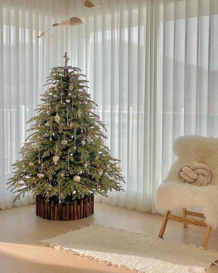 Bright beige flooring and white curtains in a living room featuring a decorated Christmas tree with wood-tone fence and beige armchair in a cozy natural modern setting