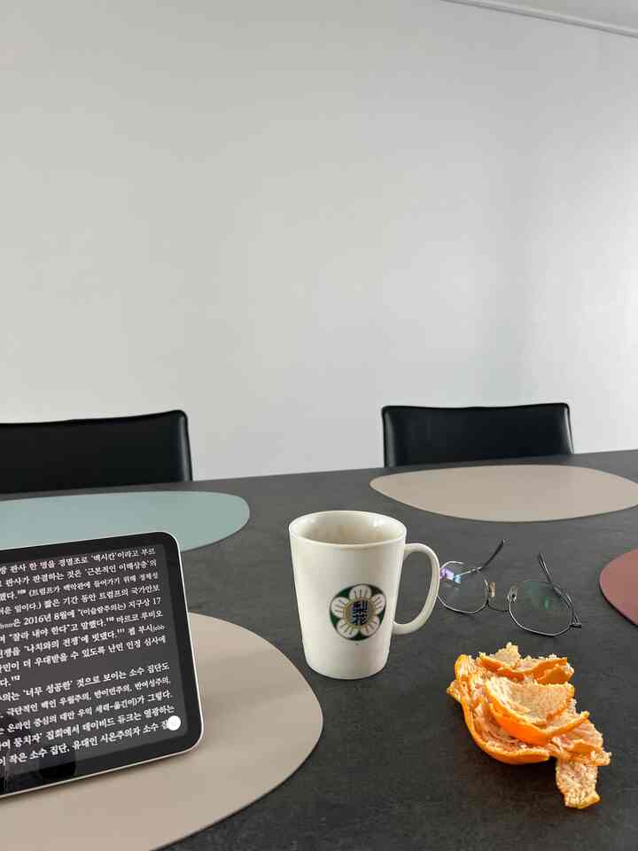 白い壁と黒いダイニングテーブルがあるダイニングスペース、カラフルなランチョンマットとコーヒーカップ、眼鏡、みかんの皮が整然と置かれた雰囲気のあるインテリア