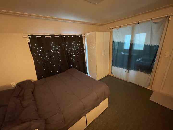 ブラウンとホワイトのトーンの寝室、遮光カーテンと白いクローゼットが配置された落ち着いた雰囲気のあるインテリア