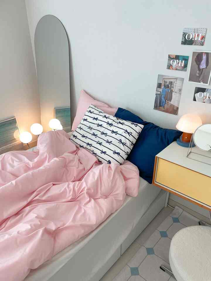 ピンクのトーンが特徴の寝室、シンプルな収納ベッドに複数の枕とテーブルランプが配置された雰囲気のある空間