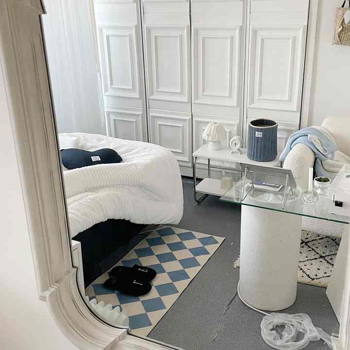 White and blue toned bedroom featuring a white fabric sofa, bed with cozy bedding, and a patterned rug creating a clean and warm atmosphere