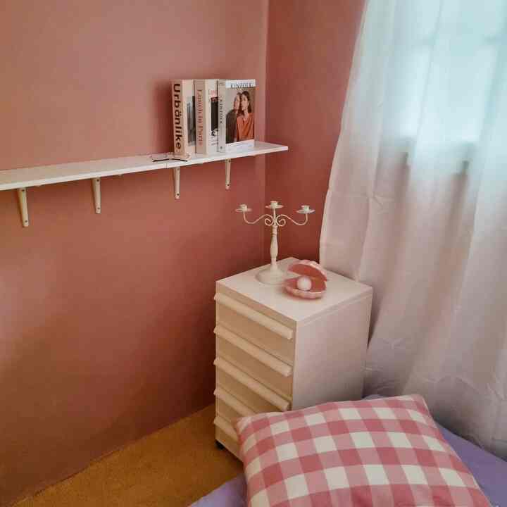 Small bedroom interior featuring pink walls, white furniture, and a checkered pillow