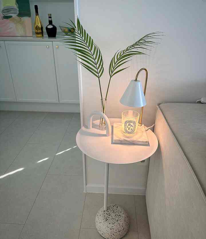 White-toned living room featuring a modern side table with candle and plant, showcasing a clean and minimal interior