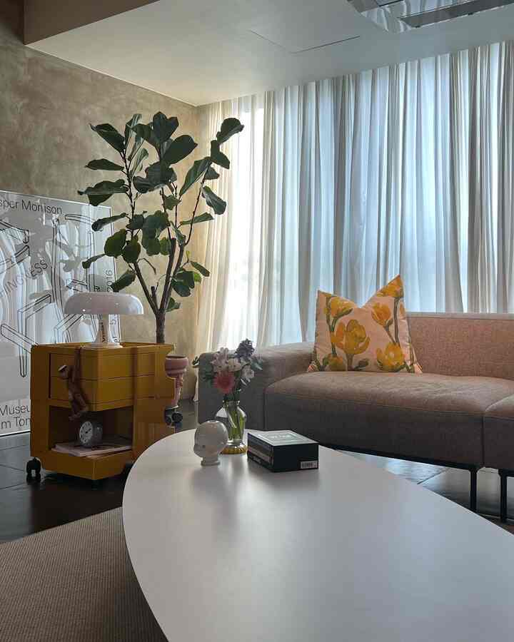 Natural style living room featuring beige walls, brown sofa, white curtains, and an oval coffee table with bright soft lighting