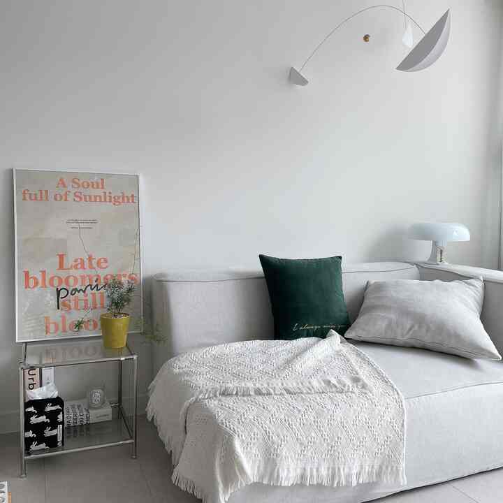 A white and green toned living room featuring a modern white sofa with cushions and throw, table lamp creating a clean atmosphere