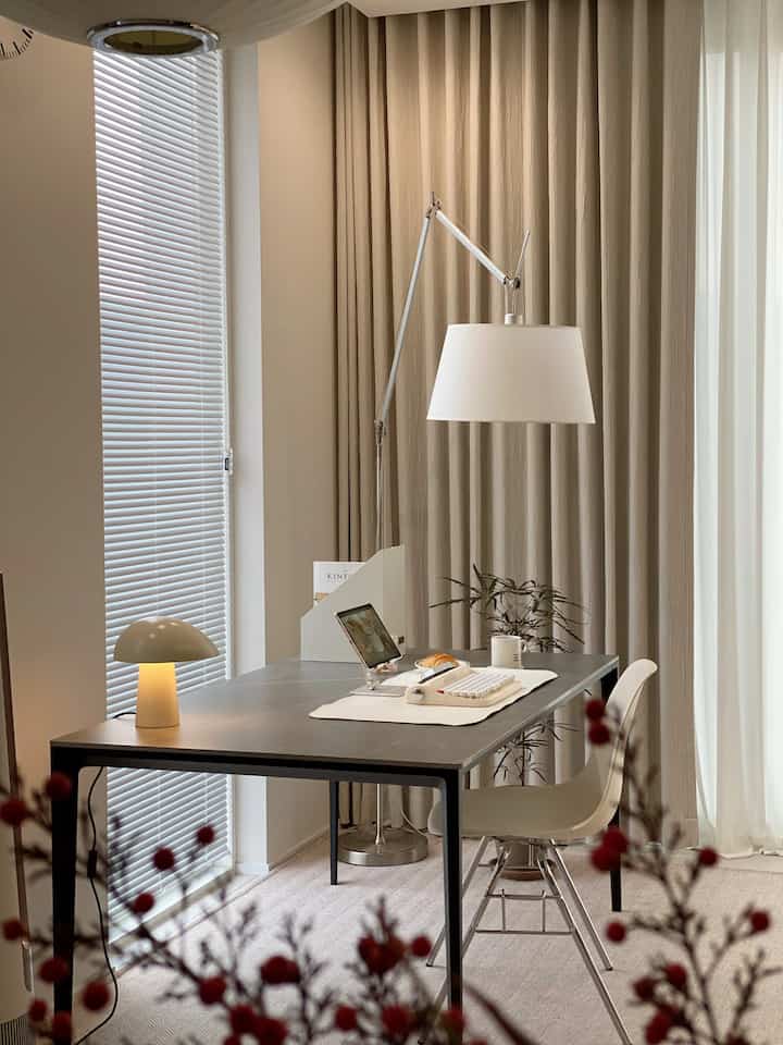 Beige and white toned home office featuring neat desk, lighting, and curtains in a modern space