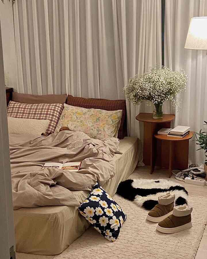 Natural beige-toned bedroom featuring a large bed with assorted pillows, wooden bedside tables, and a vase of flowers creating a cozy atmosphere