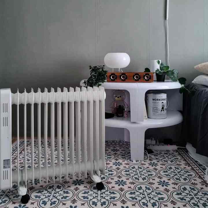 グレーの壁、白いサイドテーブル、柄の床タイル、白いオイルヒーターが配置されたモダンな空間