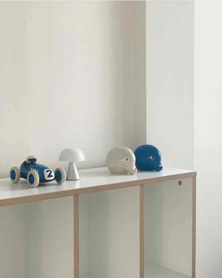 White and blue toned kids' room bookshelf topped with a toy car, table lamp, and elephant objets in a minimalist setting