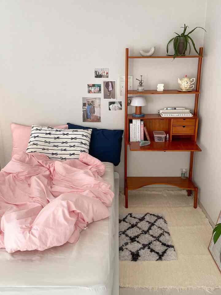 Cozy bedroom space with white walls, pink bedding, and natural wood-toned desk