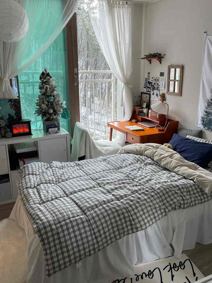 A white and navy-toned bedroom featuring a wooden desk and sheer curtains with a cozy atmosphere