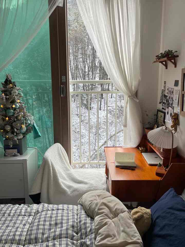 白とネイビーが調和するワンルーム寝室、コンパクトな木製デスクとカーテンが温かみのある雰囲気を演出するインテリア