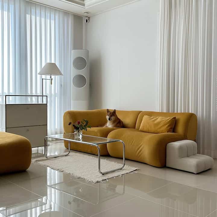 A bright white and yellow toned modern living room featuring a yellow sofa and transparent coffee table with a dog comfortably sitting
