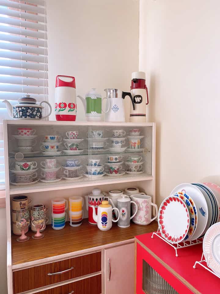 A white and wood tone vintage kitchen space featuring various colorful vintage teacups and teapots with cozy atmosphere