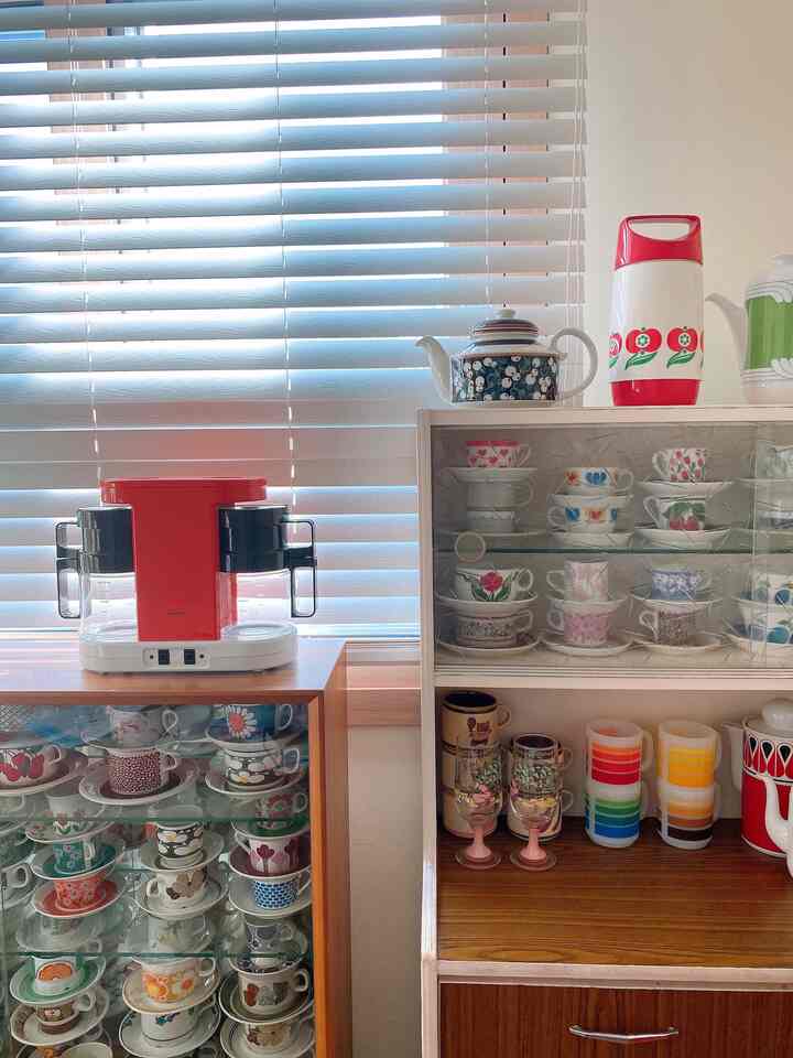 Bright wood-tone furniture showcasing red coffee machine and assorted vintage teacups in a cozy home cafe space