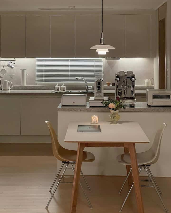 White and wood tone kitchen space featuring dining table and pendant light centrally, with a cozy and clean natural modern style