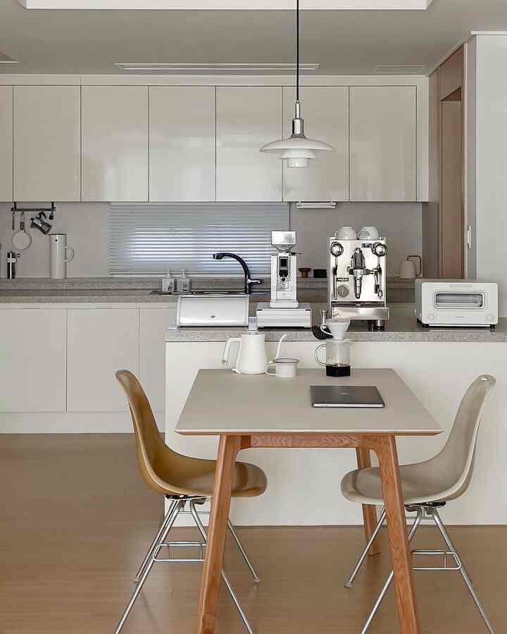 A minimal and modern kitchen and dining space for two featuring white cabinetry, wood tones, and coffee equipment