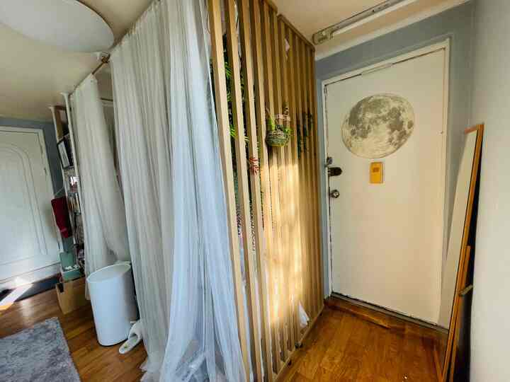White and wood tone entrance space featuring wooden slatted partition and sheer white curtains creating a cozy and open atmosphere