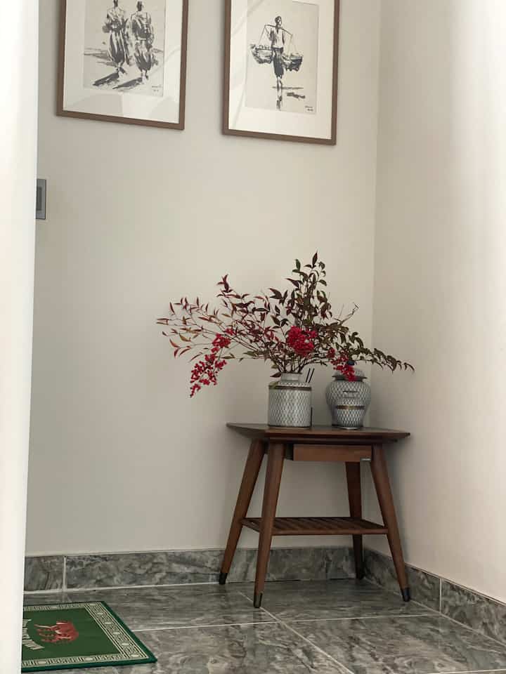 ナチュラルな木目調と白い壁の玄関の角に額装された絵とオリエンタルな花瓶が置かれた清潔感のある空間