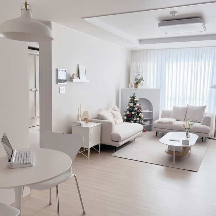 Bright natural-toned living room featuring white sofas and a round dining table with a cozy atmosphere