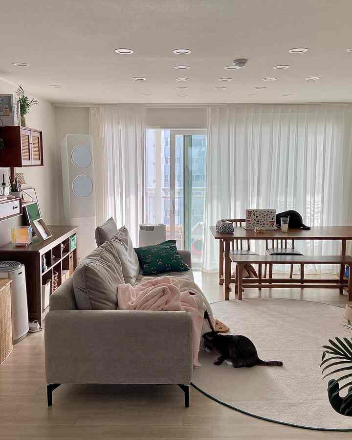 Bright natural-toned living room with wood dining table, gray sofa, and round rug arranged in a cozy interior