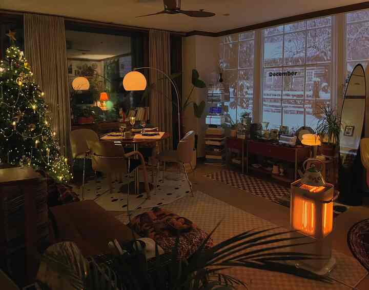 暖かい木目調と緑の植物が配されたリビング、クリスマスツリーと電気ストーブが居心地の良い冬の雰囲気を作る空間