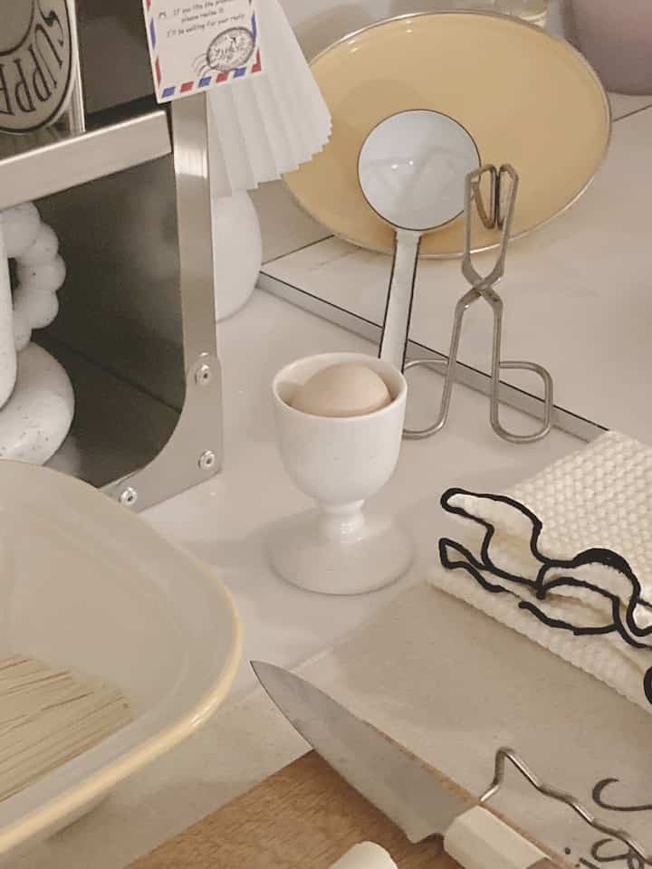 Cozy kitchen dining table in beige and white tones featuring a knife, plates, and a boiled egg in an egg cup