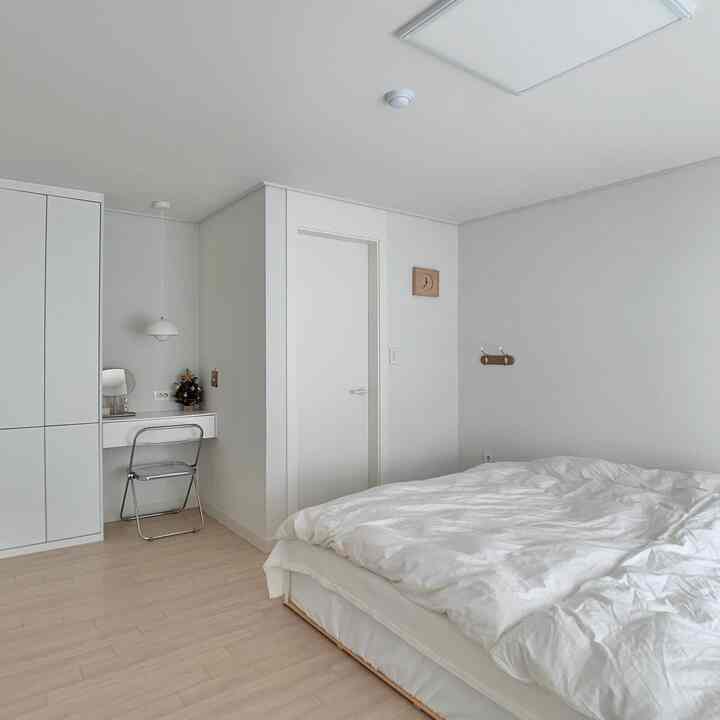 Bright white and natural wood tone bedroom featuring simple furniture and white bedding with a cozy atmosphere