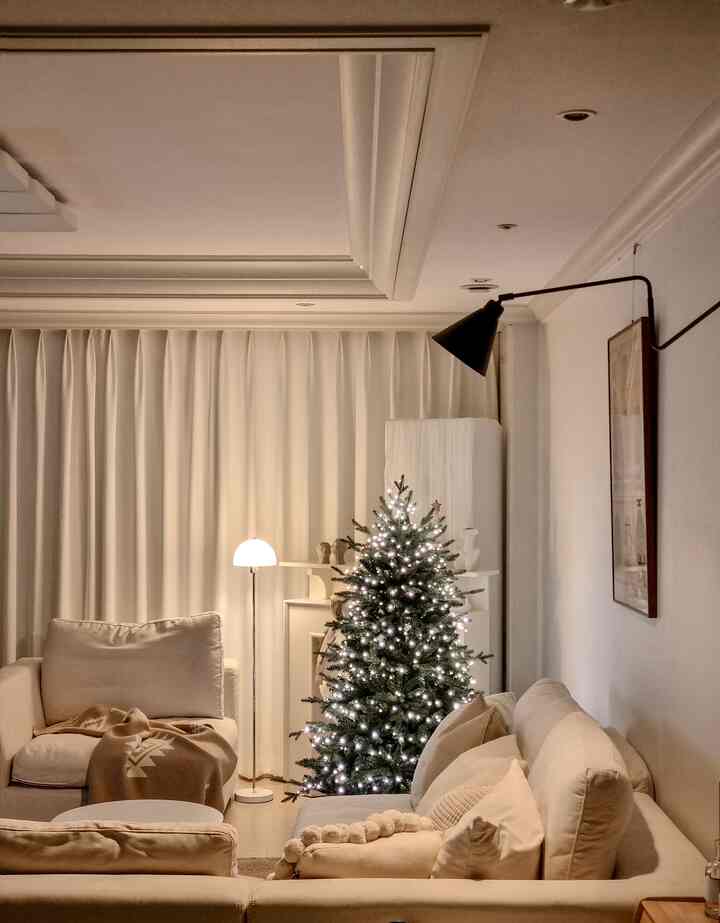 Cozy living room in soft ivory and beige tones featuring a Christmas tree decorated only with string lights