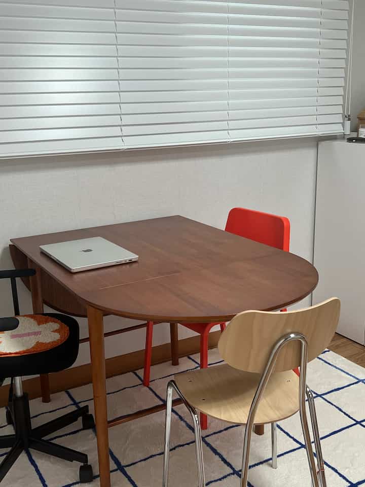 ホワイトのブラインドと木目調のダイニングテーブル、多様な椅子が配置されたミッドセンチュリーモダンなヴィンテージ感のあるコンパクトなダイニングルーム