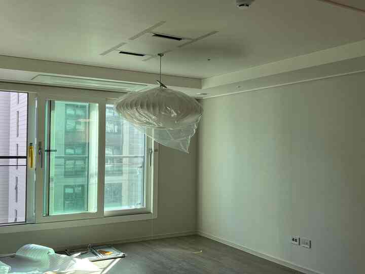 White and gray toned studio apartment living room featuring a centrally hung bubble pendant light covered with plastic wrap, minimalistic space